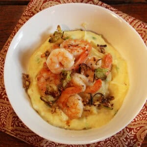 Shrimp and creamy grits topped with crisped scallions in a white bowl.