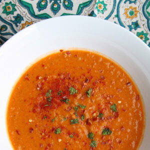 Bowl of Turkish red lentil soup dusted with paprika and chile flakes, patterned cloth behind.