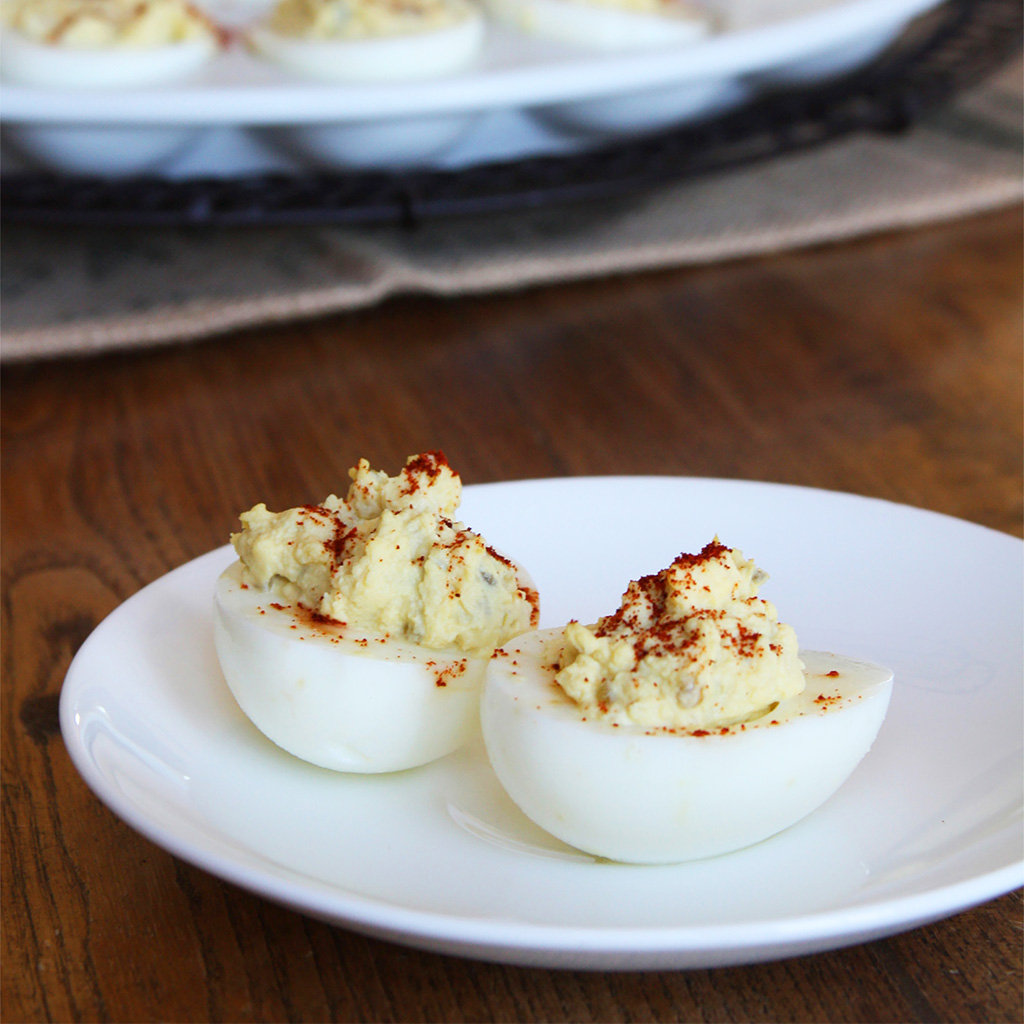 Two deviled eggs dusted with paprika on a small white plate, a full platter behind them.