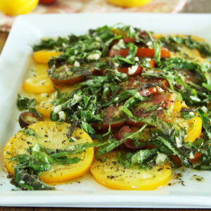 Heirloom yellow and red tomato salad layered with basil and herbed dressing on a square white plate.