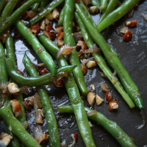 Blistered green beans in a skillet with caramelized shallots and chopped toasted hazelnuts.