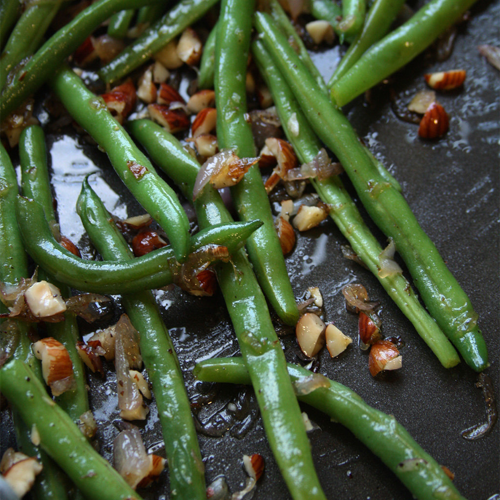 Blistered green beans in a skillet with caramelized shallots and chopped toasted hazelnuts.