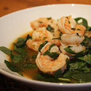Hot and sour Thai shrimp soup with basil leaves, cilantro, and spinach in a shallow white bowl.