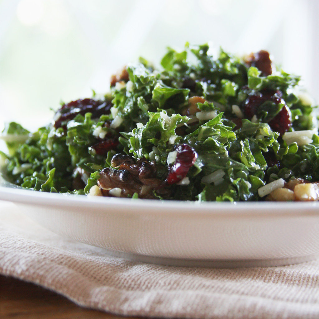 Chopped kale salad with dried cranberries, walnuts and shredded parmesan cheese heaped in a white bowl.