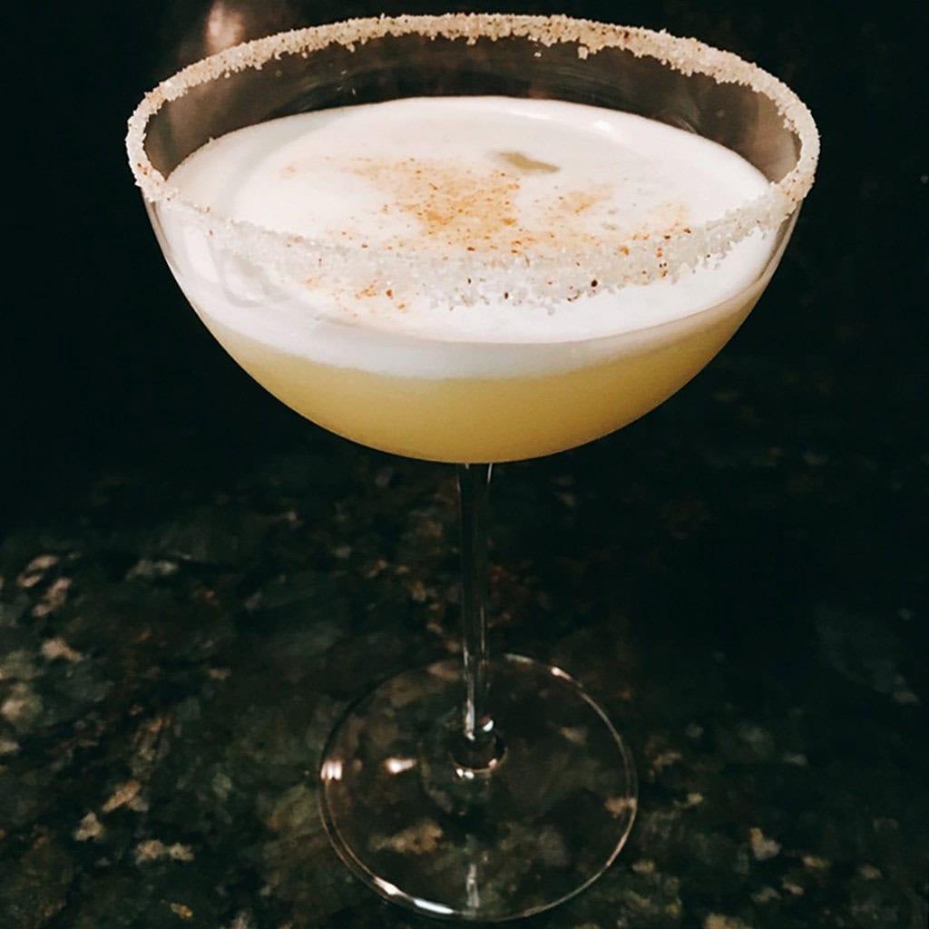 Mother of Dragons cocktail with a thick foam cap, grated spice and a sugared rim in a coupe glass.