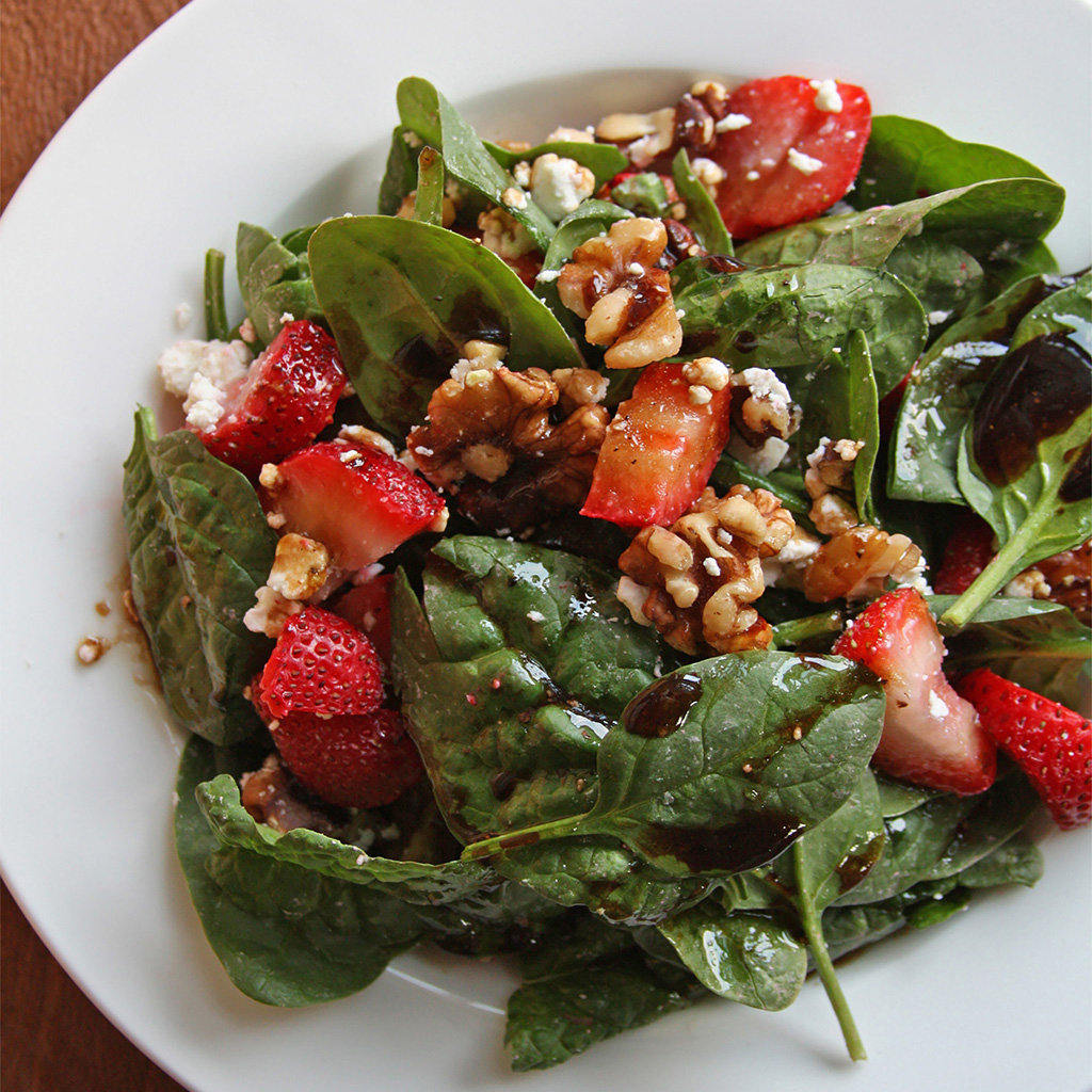 Spinach and strawberry salad with walnuts, goat cheese and balsamic vinaigrette on a white plate.