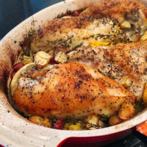 Roasted lemon garlic chicken breasts with lemon and thyme in a cream baking dish.
