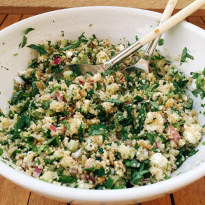 Summer French couscous with parsley, mint, cucumber and feta being tossed in a large white bowl.