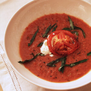 Bowl of balsamic roasted tomato soup topped with burrata, a roasted tomato slice and torn basil.