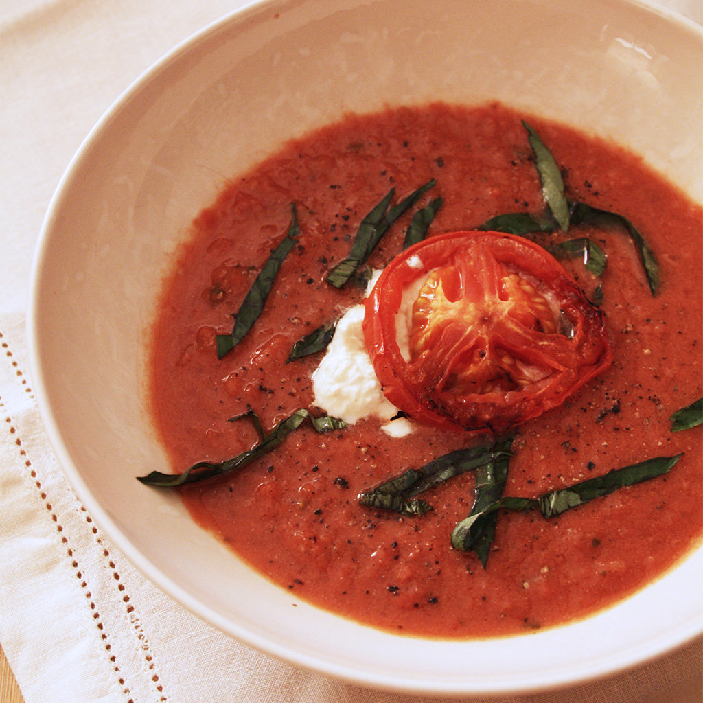 Bowl of balsamic roasted tomato soup topped with burrata, a roasted tomato slice and torn basil.