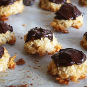 Coconut macaroons dipped in dark chocolate cooling on parchment paper.