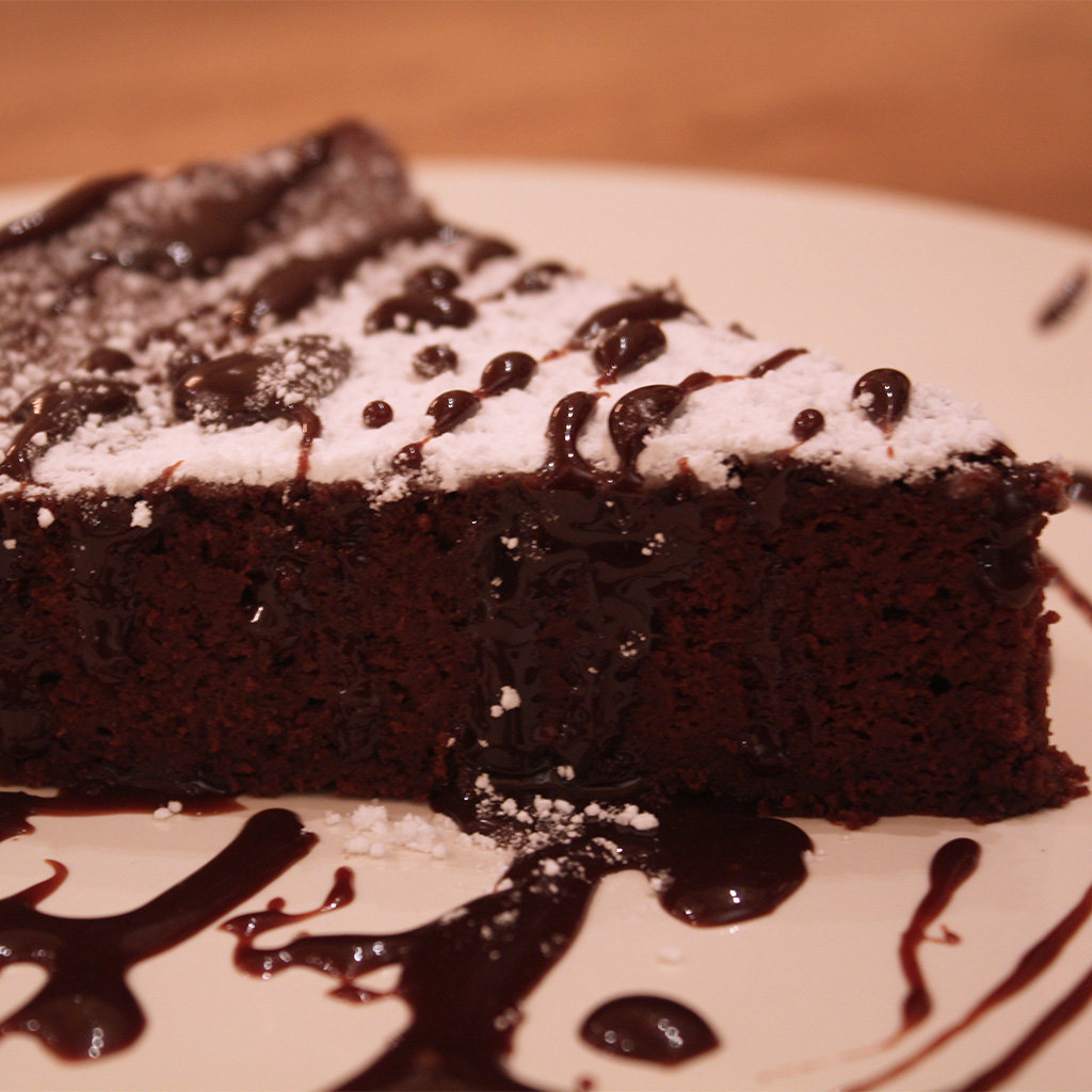 Wedge of dense flourless chocolate cake dusted with powdered sugar and drizzled with chocolate sauce.