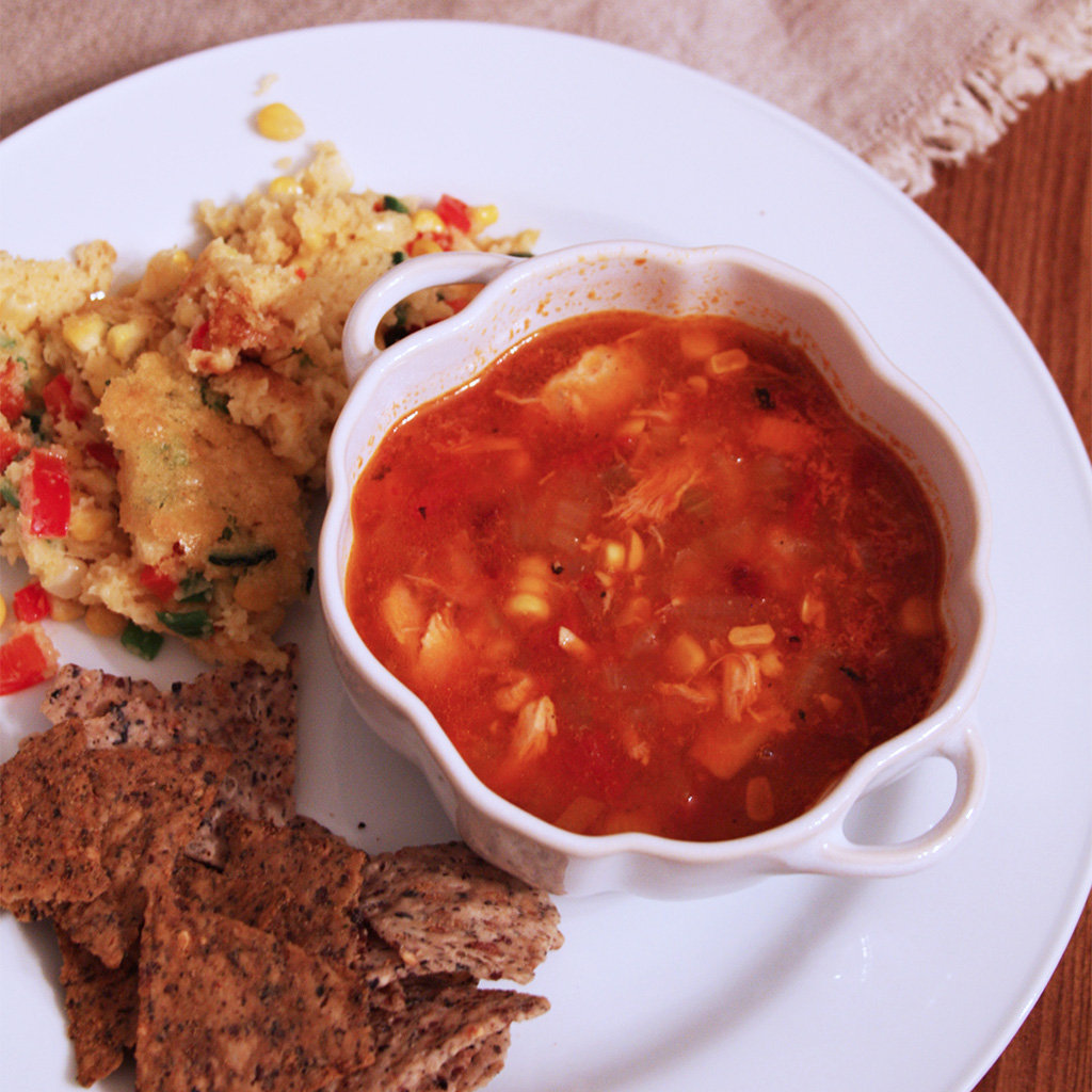 Corn and chicken tortilla soup in a white crock with corn pudding and blue corn tortilla chips.