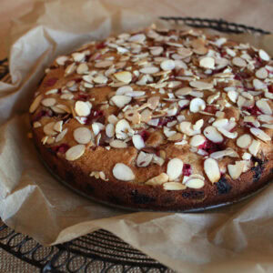 Cranberry almond cake topped with toasted sliced almonds, cooling on parchment over a wire rack.