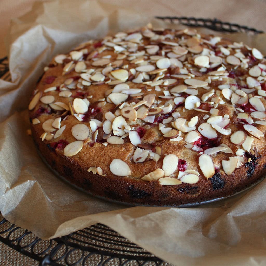 Cranberry almond cake topped with toasted sliced almonds, cooling on parchment over a wire rack.