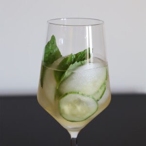 Cucumber basil cooler in a stemmed glass with cucumber slices, basil leaves and ice.