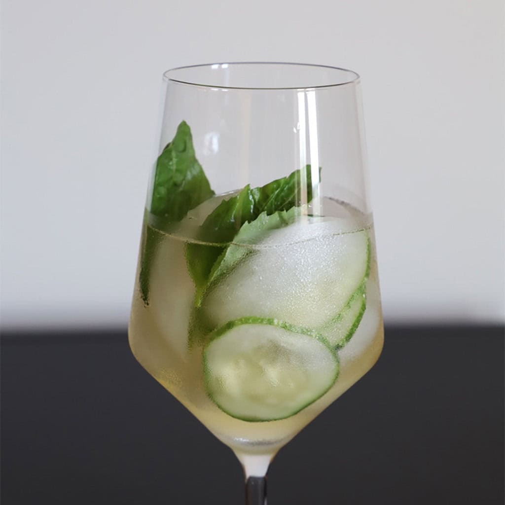 Cucumber basil cooler in a stemmed glass with cucumber slices, basil leaves and ice.