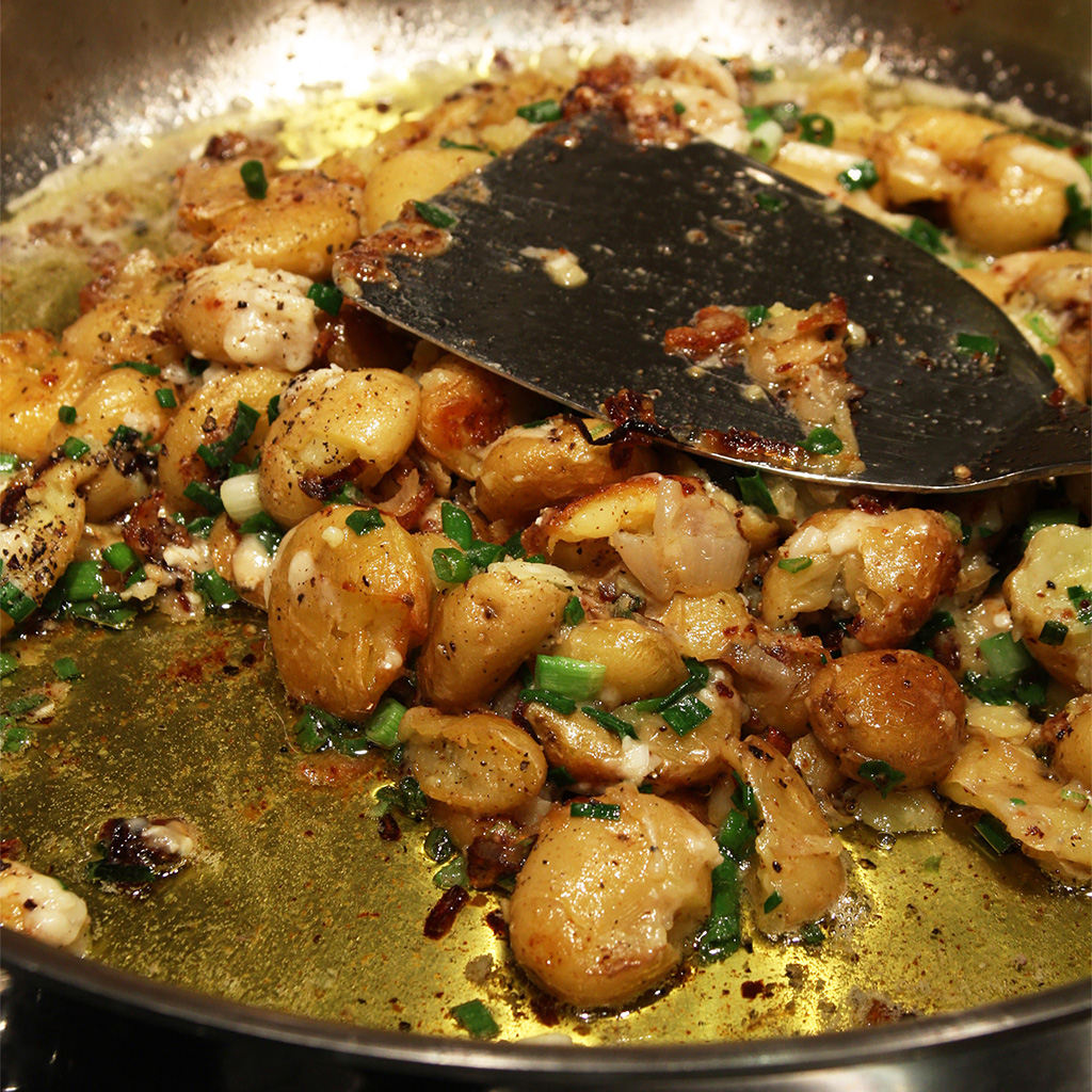 Smashed baby potatoes crisping in a skillet with garlic, scallions and butter.