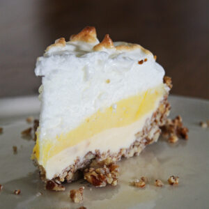 Slice of lemon meringue ice cream pie with torched meringue peaks and a toasted pecan crust.