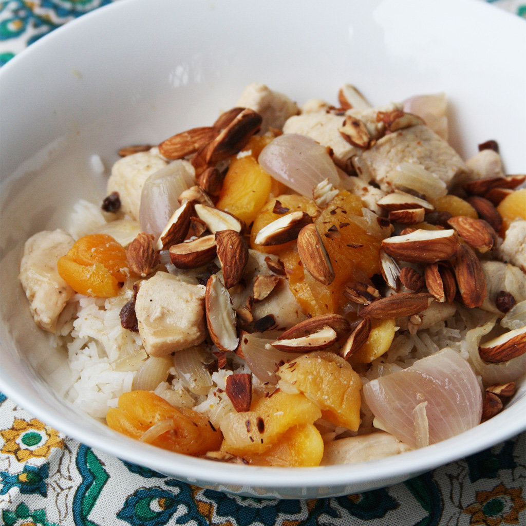 Mahmudiye chicken with dried apricots, shallots and sliced almonds over rice in a white bowl.