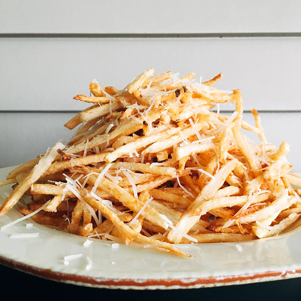 Tall pile of shoestring pomme frites showered with shaved parmesan on a rustic plate.