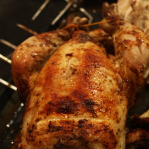 Whole rotisserie chicken with crisp golden paprika-rubbed skin turning on the spit.