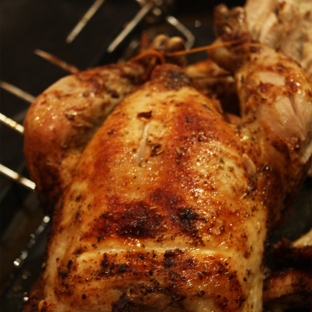 Whole rotisserie chicken with crisp golden paprika-rubbed skin turning on the spit.