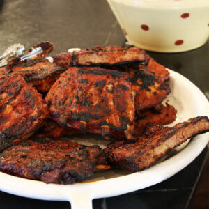 Charred lacquered pork ribs glazed in spicy Korean barbecue sauce piled on a white platter.