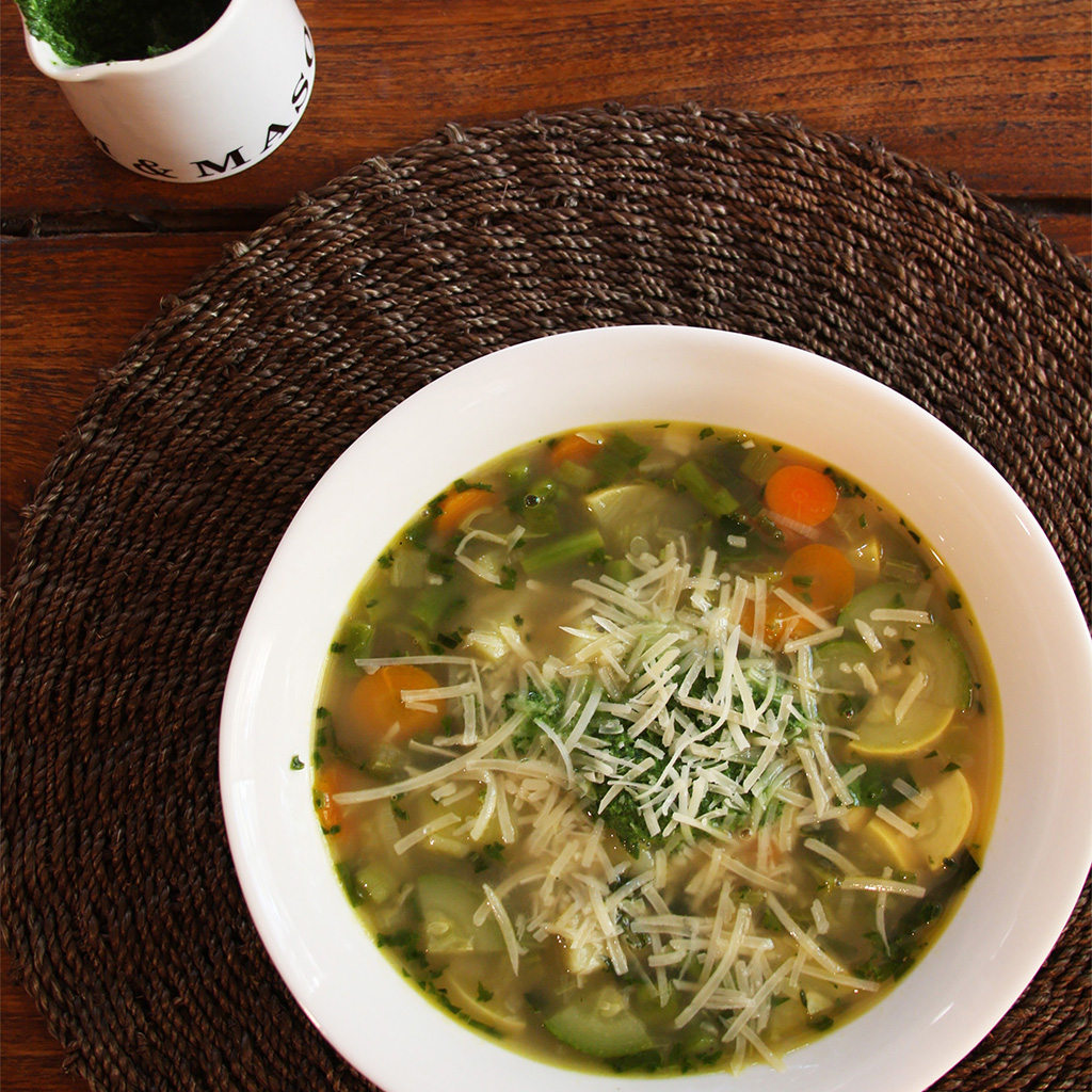 Spring vegetable soupe au pistou with squash and carrots under shredded parmesan, pistou jar behind.
