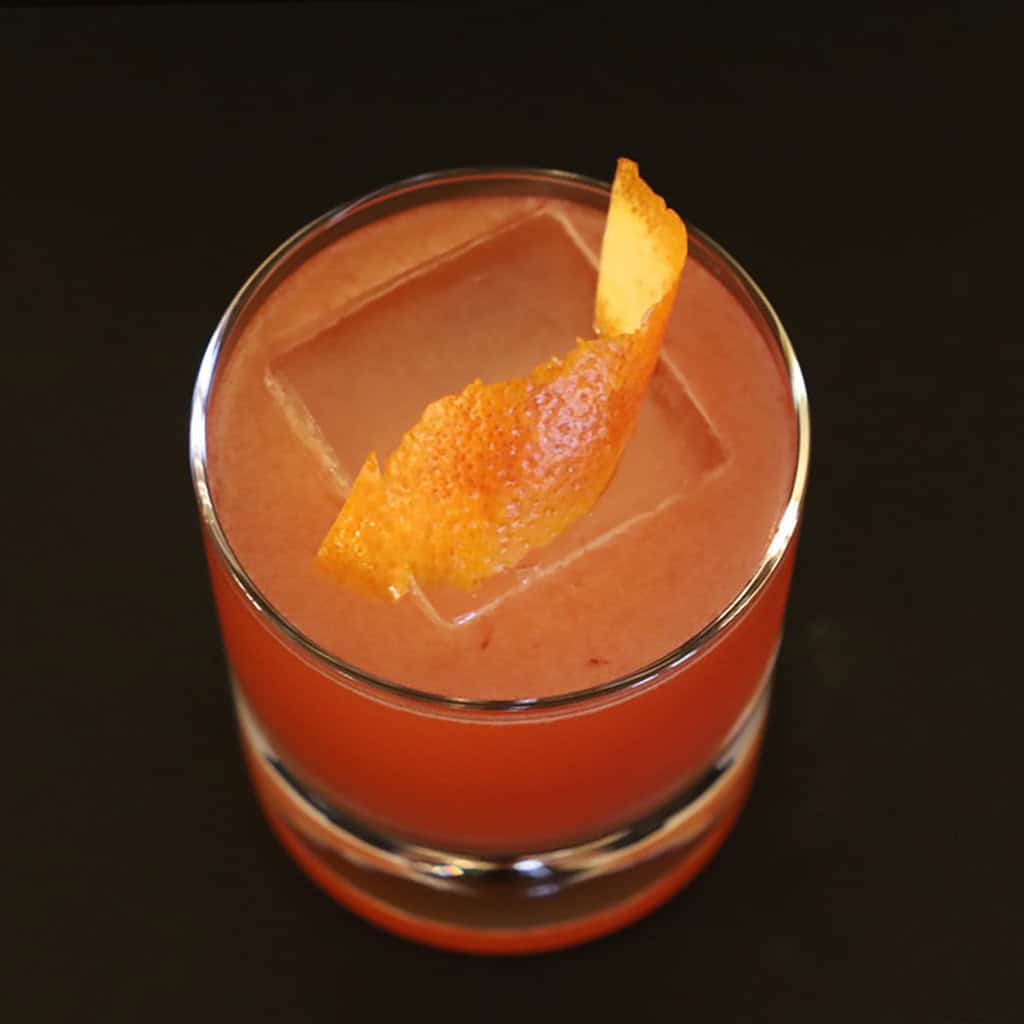 Overhead view of The Nameless cocktail with a curled orange peel resting on the ice cube.