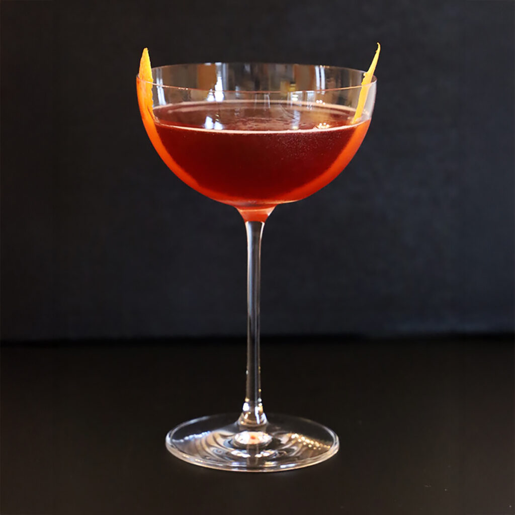 Fernegroni cocktail in a coupe glass with orange peel garnish against a black background.