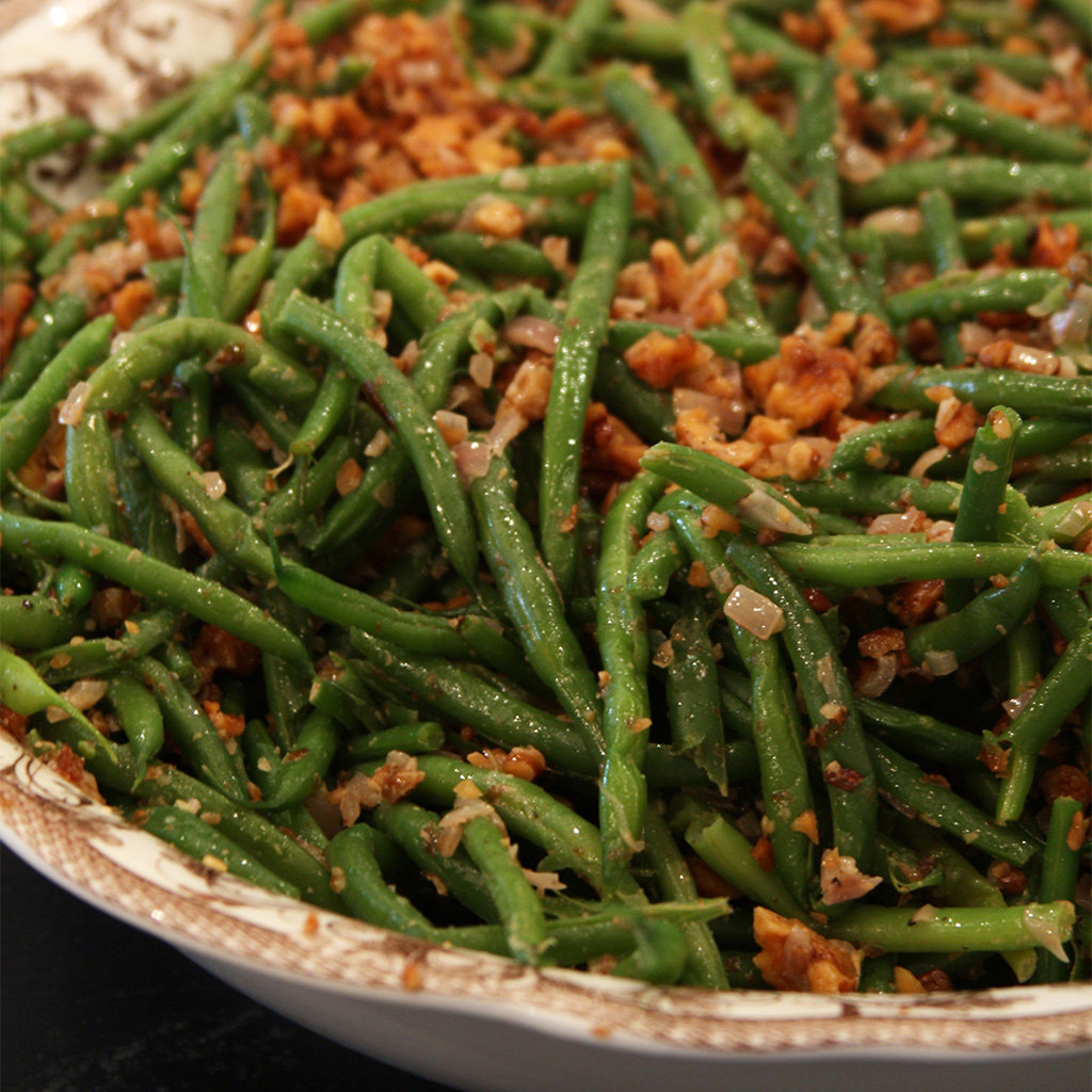Green beans tossed with crisped bacon, shallots and toasted pecans in a rustic serving bowl.