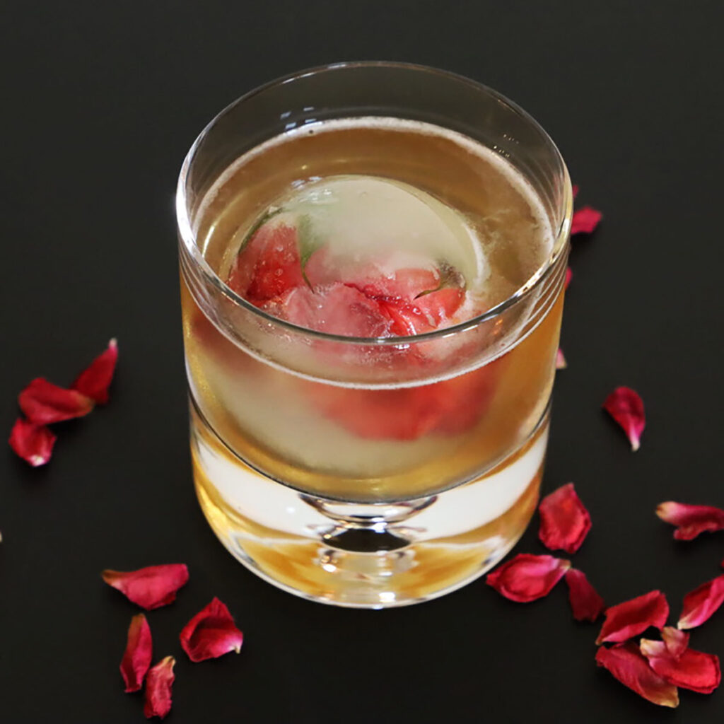 Run for the roses whisky and rose water Manhattan cocktail against a black background with a rose ice cube.
