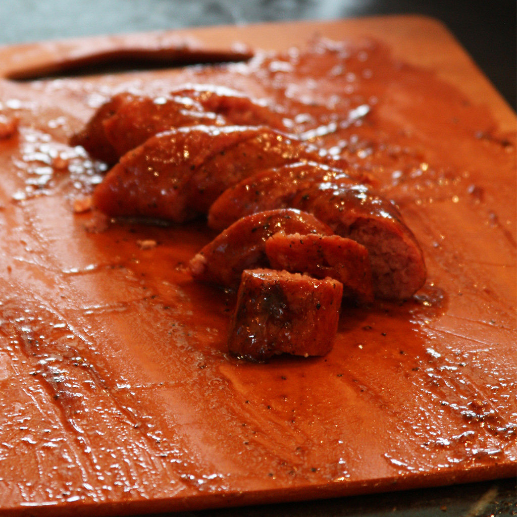 Slow-cooked sausage sliced on a well-seasoned wooden cutting board.