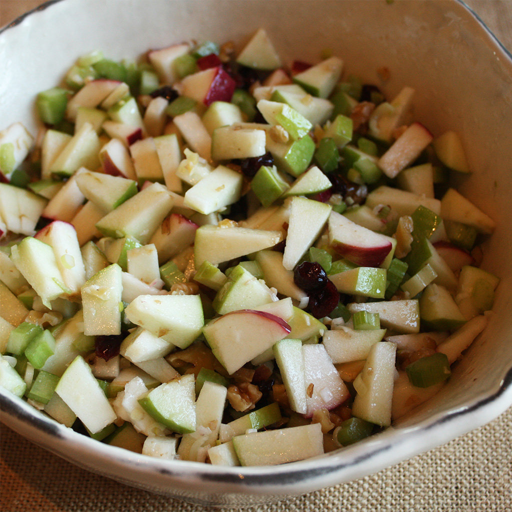 Waldorf salad of diced red and green apple, celery, walnuts and dried cranberries in a rustic bowl.