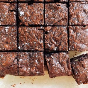 Overhead view of keto almond butter walnut brownies cut into squares on parchment, crackly tops flecked with flaky salt.