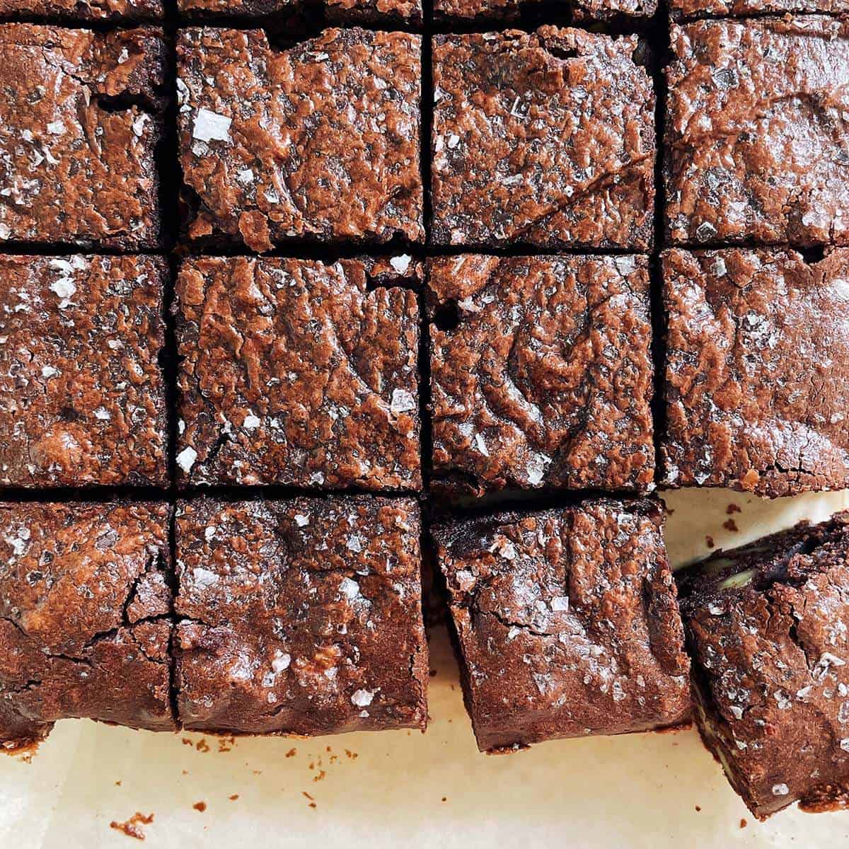 Overhead view of keto almond butter walnut brownies cut into squares on parchment, crackly tops flecked with flaky salt.