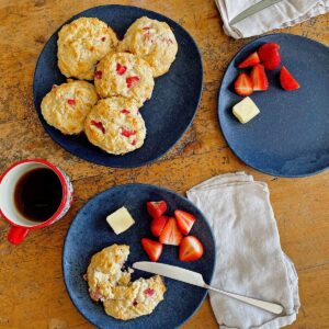 Keto strawberry almond drop biscuits on a black plate, one split on a second plate with butter, strawberries and coffee.